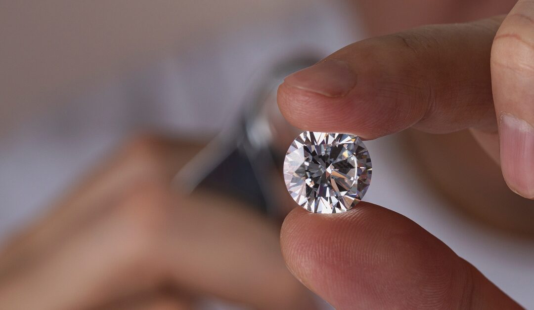 Close-up of the hand of a man holding a large, round, shiny diamond with multiple clean cuts with his fingertips.